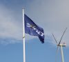 Eine Svolt Fahne vor blauem Himmel mit einem Windrad im Hintergrund.