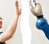 Eine menschlicher Mitarbeiter setzt zum High-Five mit einem Roboterarm an.