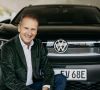 VW-Chef Herbert Diess kniet lächelnd vor einem VW.